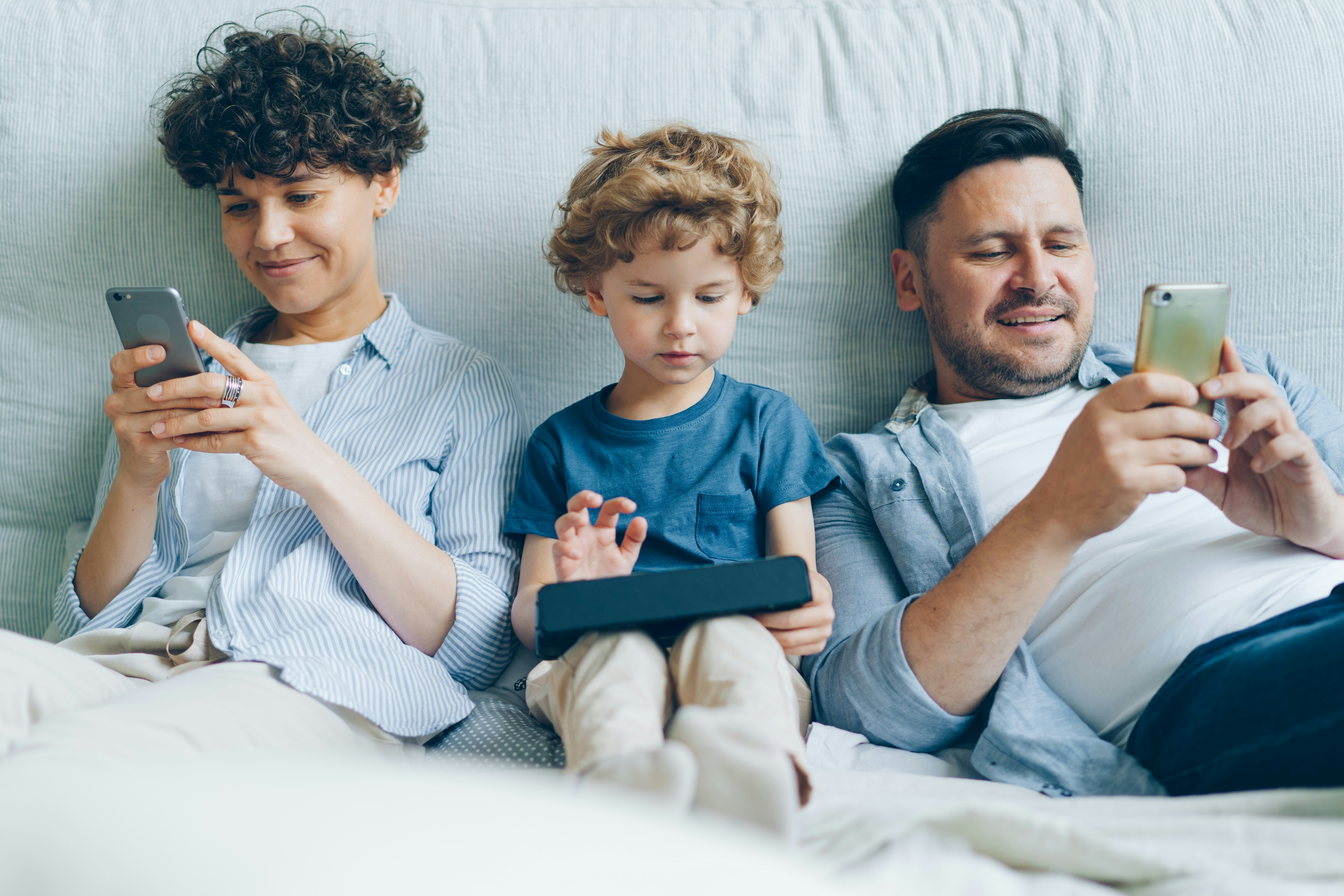 Vater liegt mit seinen zwei Söhnen im Bett und alle schauen aufs Handy